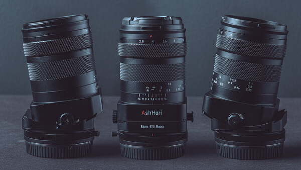 Three vintage manual focus lenses arranged side by side, displaying their barrels, focus rings, and aperture scales against a gray background.