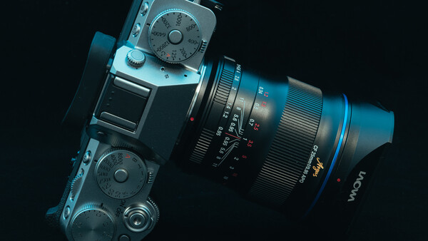 Blue mirrorless camera with attached zoom lens positioned diagonally against a black background.