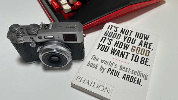 Rangefinder camera next to open book with motivational quote and red digital keyboard in background.