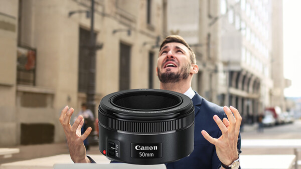 Man holding a Canon 50mm lens toward camera on an urban street.
