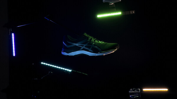 Neon light painting setup with glowing tubes and illuminated running shoe against dark background.