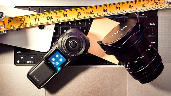 Photography gear and tech accessories arranged flat with measuring tape, including a compact camera, telephoto lens, smartwatch, and keyboard.