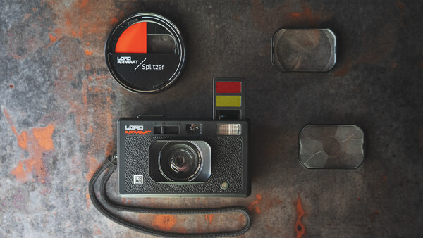 Vintage film camera with lens cap, light meter, color checker, and lens filters arranged on a weathered metal surface.