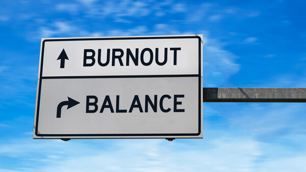 Road sign with two directional options: burnout pointing upward and balance pointing right, set against a blue sky.