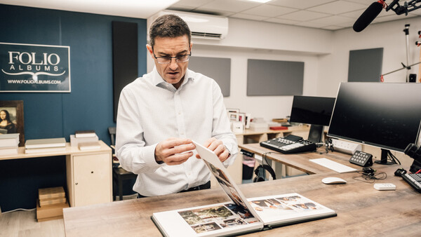 Man in white shirt examining open portfolio books at wooden desk in studio.