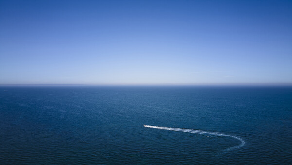 Aerial view of a speedboat leaving a curved wake across calm blue ocean water.