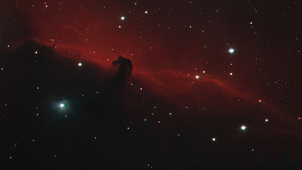 Deep-space photograph showing a dark nebula silhouetted against red hydrogen emission clouds and scattered stars.