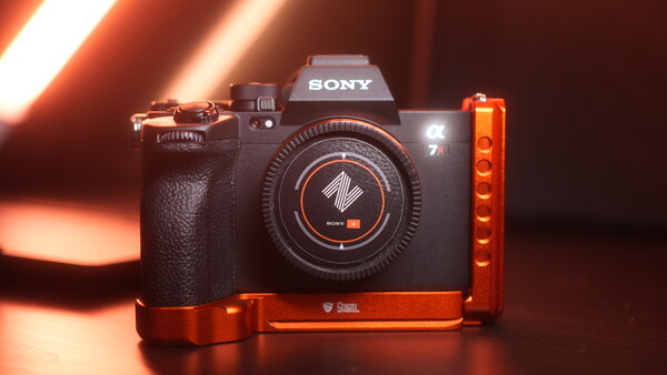 Sony mirrorless camera with red L-bracket mounted on dark surface under warm studio lighting.