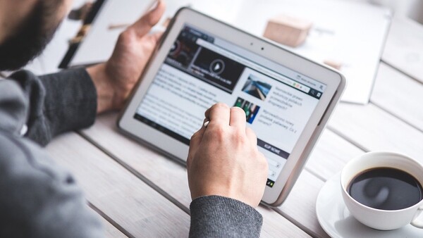Person using tablet to view a website with video content and articles at a desk workspace.
