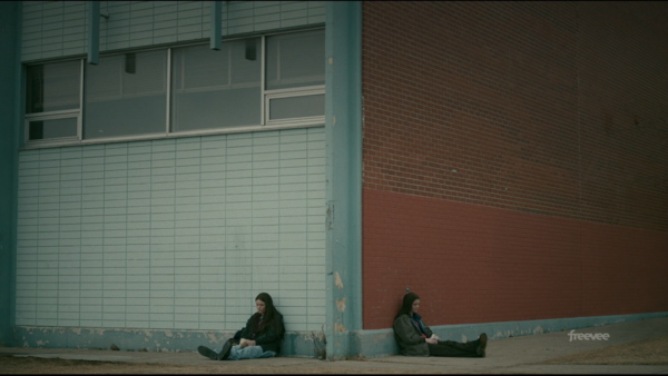 Two people sitting separately against a colorful urban wall with turquoise and rust tones.