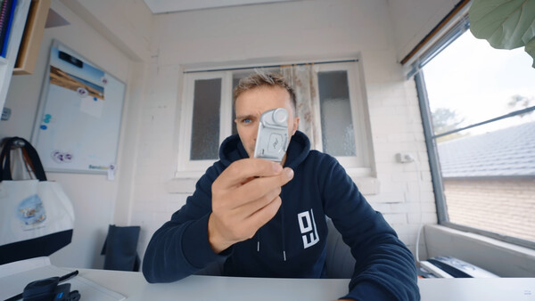 Person holding a smartphone displaying a selfie, shot from a wide angle in a bright interior space.