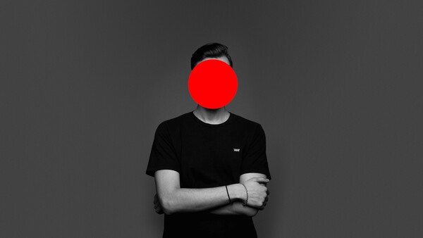Person in black t-shirt with arms crossed, face obscured by large red circle.