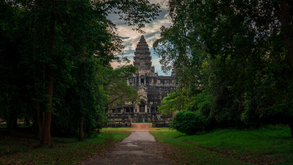 Ancient stone temple tower framed by tree-lined pathway in verdant garden setting.