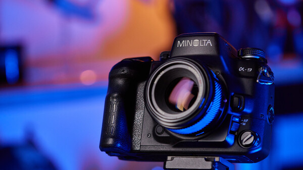 Minolta α-9 camera with blue accent lighting against a colorful bokeh background.