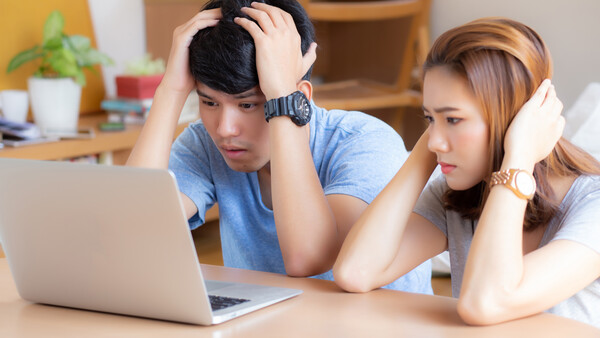 Two young people looking at a laptop screen together with concerned expressions in a home office setting.