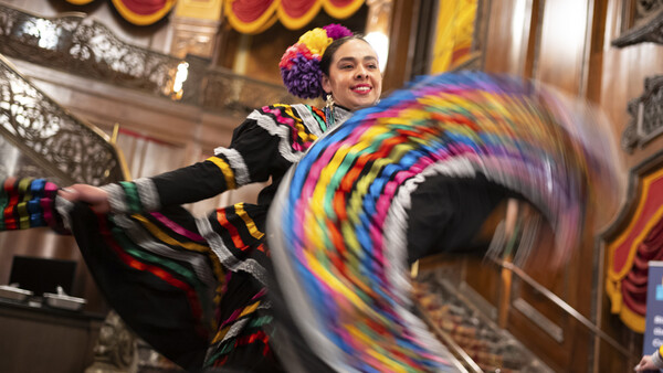 Performer in colorful striped costume spinning a rainbow hula hoop indoors.