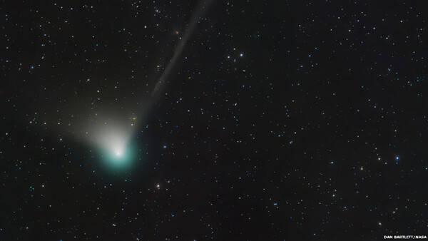 Comet with bright greenish coma and dust tail against starfield.