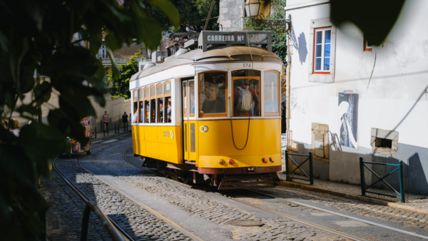 Yellow and cream vintage tram on narrow cobblestone street lined with white buildings.