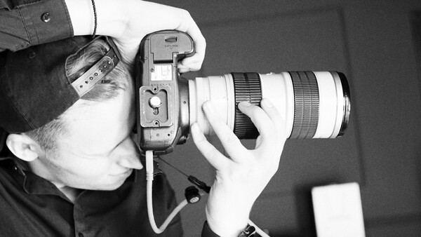 Photographer holding a mirrorless camera with a telephoto lens to their face while shooting.