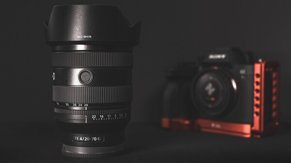 Fast prime lens with f/4.20-70°C specifications displayed on barrel, positioned in sharp focus against blurred camera and red lighting rig.