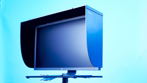 Professional color reference monitor with hood displayed against a cyan background.