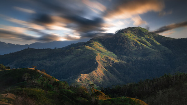 Dramatic mountain landscape with layered peaks bathed in golden sunlight under a moody sky.
