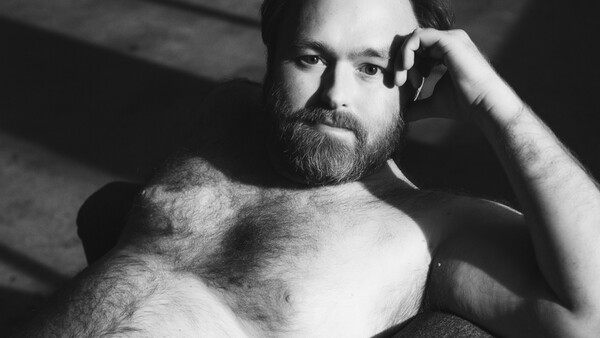 Bearded man in black and white portrait with hand to head, dramatic side lighting.