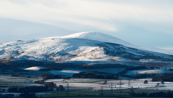Snow-capped mountain dominating a winter landscape with forested valleys and agricultural fields below.