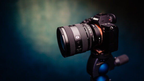 Mirrorless camera with wide-angle lens mounted on tripod against blurred teal and dark background.