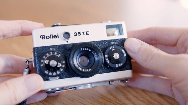 Hands holding a Rollei 35 TE rangefinder camera with white and black body.