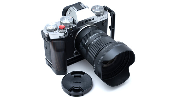 Fujifilm mirrorless camera with Sigma zoom lens, lens cap, and hood arranged on white background.