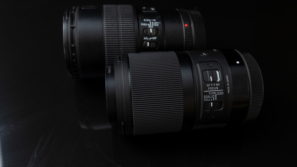 Two black telephoto lenses arranged on a dark surface against a black background.