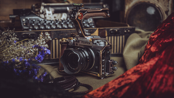Medium format camera with lens positioned among vintage photography equipment and dried flowers in warm, moody lighting.