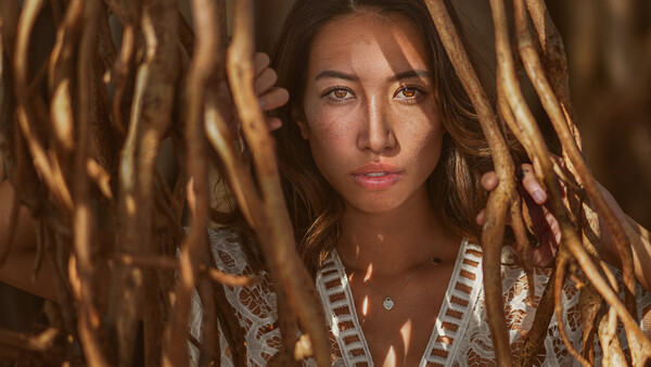 Woman with dark hair framed by dried grass, wearing a white textured top and looking directly at camera.