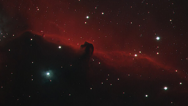 The Horsehead Nebula, a dark dust cloud silhouetted against glowing red hydrogen gas with scattered stars throughout the field.