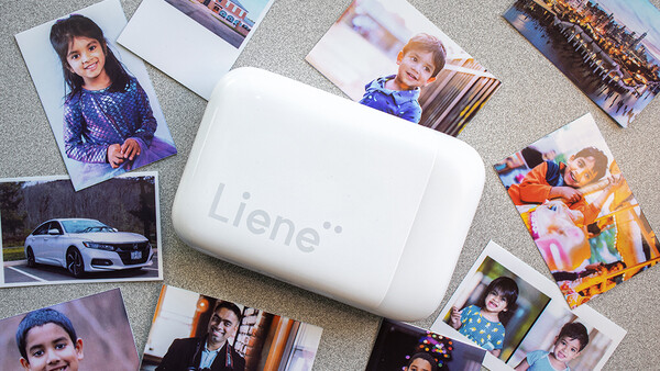 Portable photo printer surrounded by printed photographs on a textured surface.