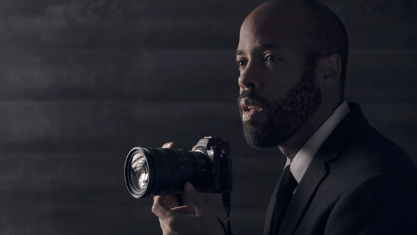 Professional photographer in business attire holding a DSLR camera with flash attachment.