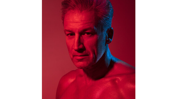 Portrait of a man with styled hair against a red and blue split-tone background.