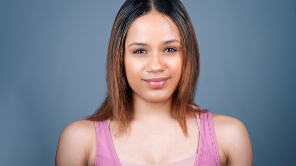 Woman with long dark hair wearing a pink tank top against a blue-gray backdrop.