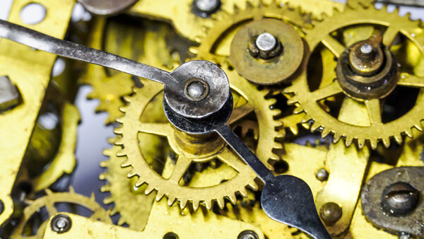 Close-up of brass watch movement gears and escape wheel lever against yellow metal plates.