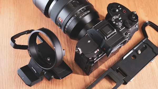 Sony mirrorless camera with attached lens, lens hood, and mounting bracket on wooden surface.