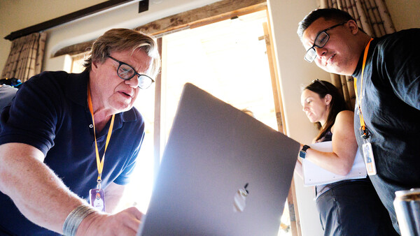 Three people gathered around a laptop computer indoors, examining the screen together.