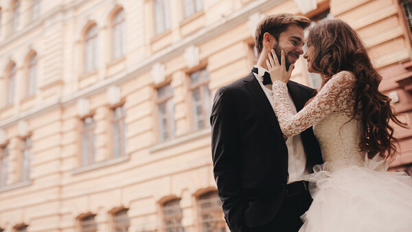 Bride and groom embracing in front of a classical building facade during golden hour.