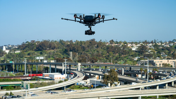 Drone hovering above a multi-level highway interchange with dense urban development in the background.