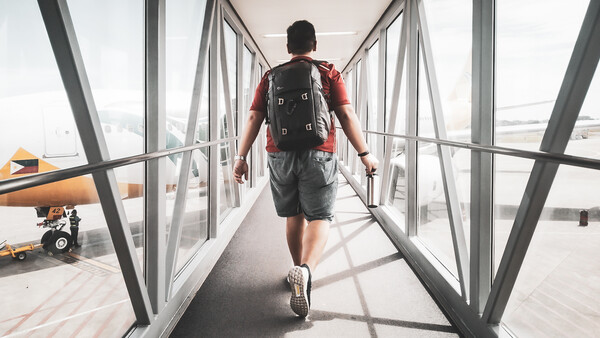 Runner jogging through a glass-walled airport jet bridge toward an airplane.