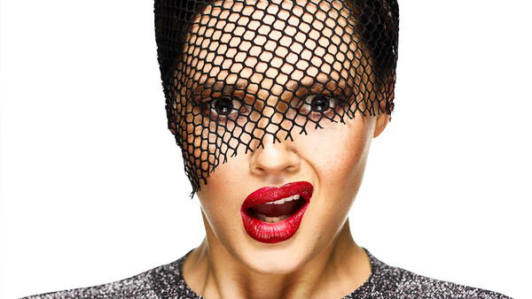 Portrait of a person wearing a black mesh veil covering the eyes, with bold red lipstick and a sparkly dark top against a white background.