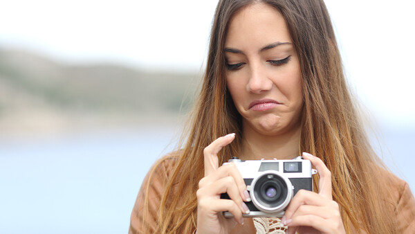 Woman holding a vintage rangefinder camera while looking down at the viewfinder outdoors.