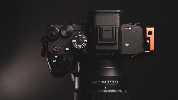 Overhead view of a mirrorless camera with electronic viewfinder, grip extension, and telephoto lens on black surface.