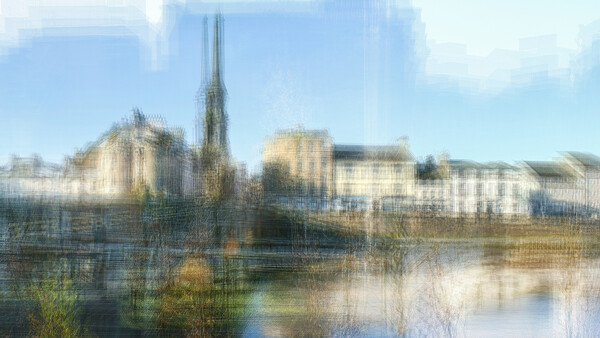 Medieval cathedral with tall spire reflected in calm river water, surrounded by historic buildings.