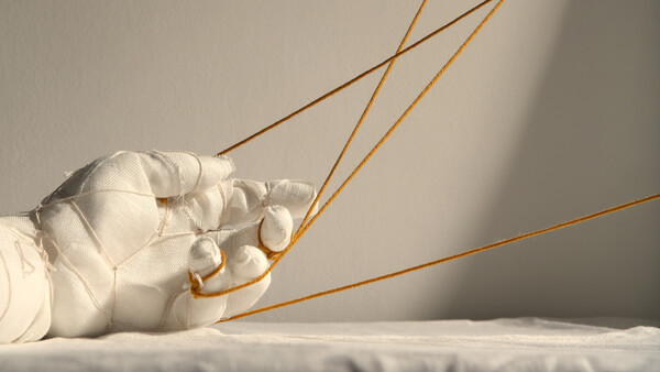 White-gloved hand holding golden strings against a neutral background with dramatic side lighting.